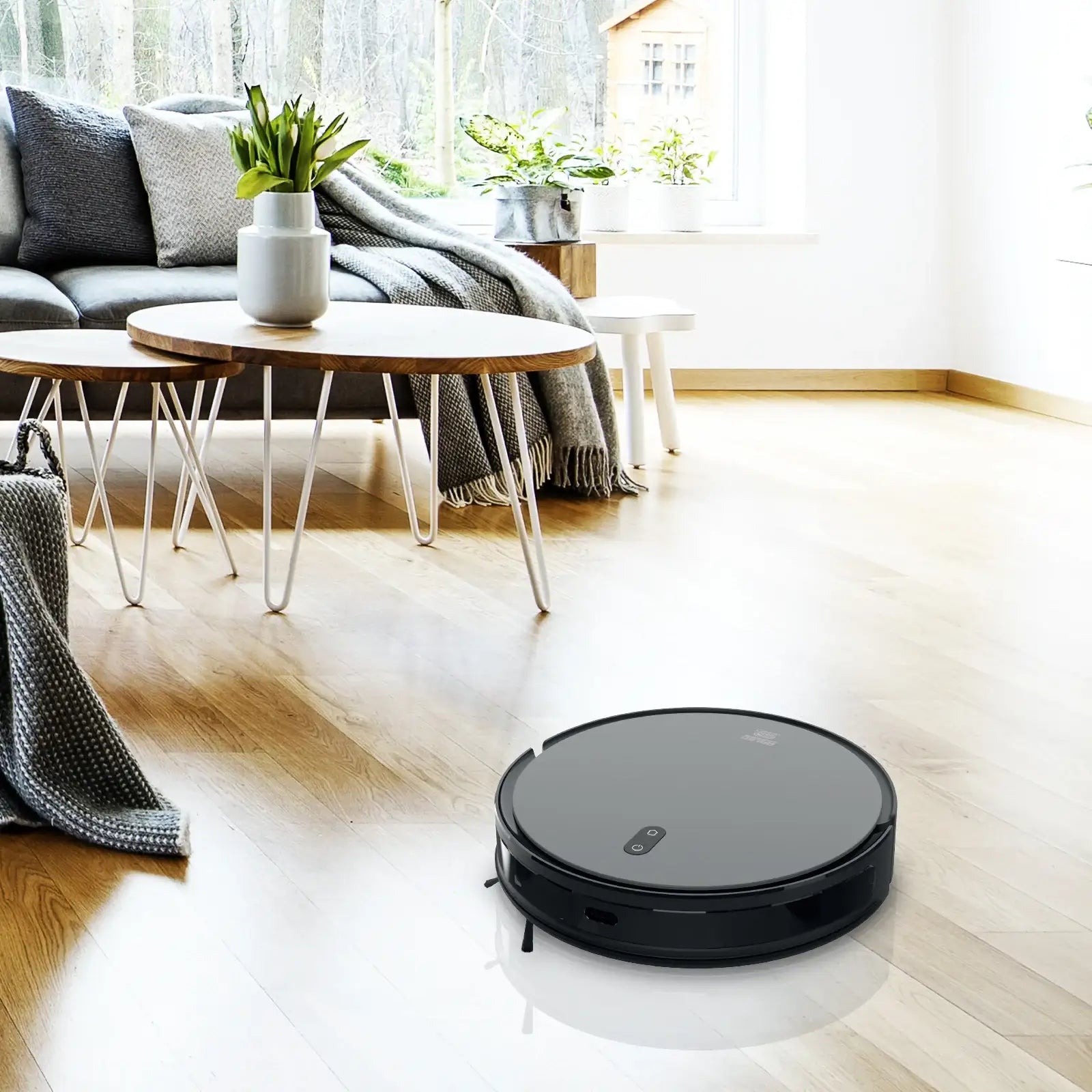 Black robot vacuum cleaner on light wood floor in modern living room