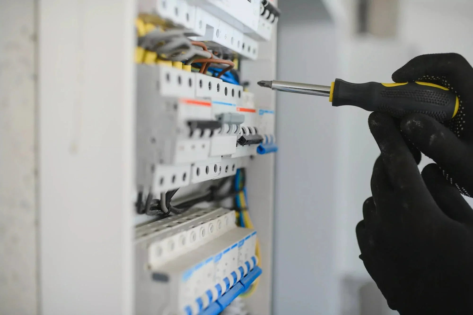 Electrician working on switchboard wiring with screwdriver and gloves